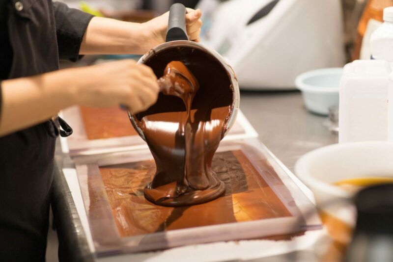 production, cooking and people concept - confectioner filling mold with chocolate at confectionery shop